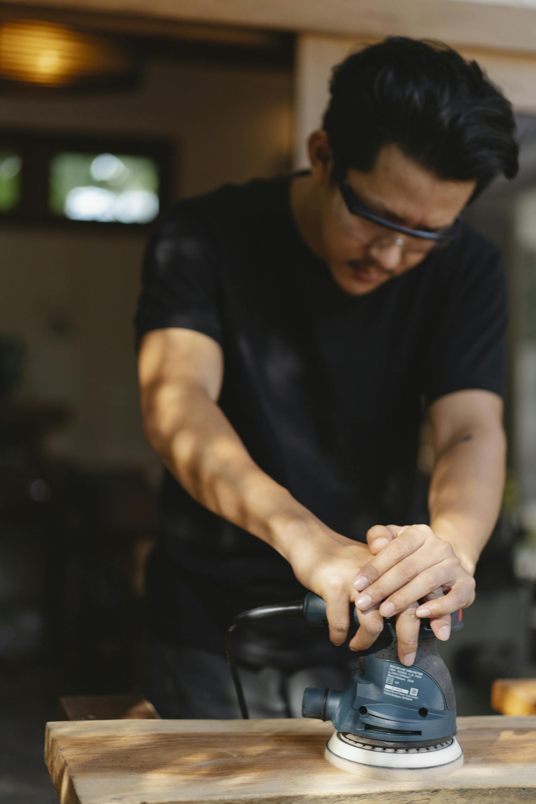 Focused carpenter using an electric sander on wood in a well-lit workshop.